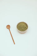 Green leaf powder in a ceramic bowl with a wooden spoon