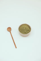 Green leaf powder in a ceramic bowl with a wooden spoon
